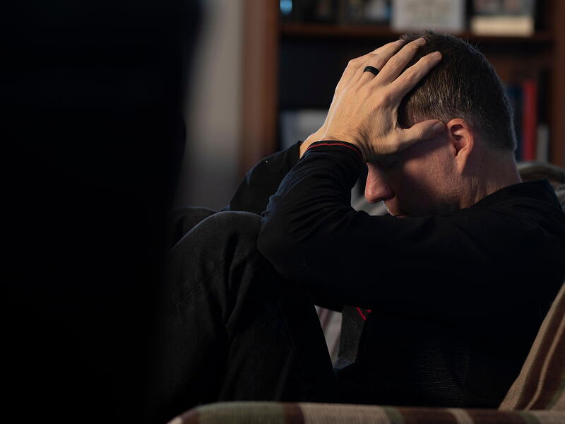 Homme assis, la tête entre les mains, dans une pièce sombre